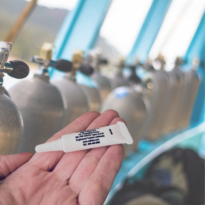 Hand holding a 5 gram tube of Christo-Lube in front of oxygen cylinders. 