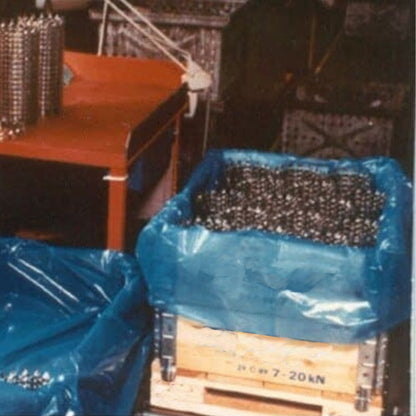 An industrial work station. To the right, a wood crate lined with VpCI-126 anti rust gusseted bags containing a large quantity of metal pieces.